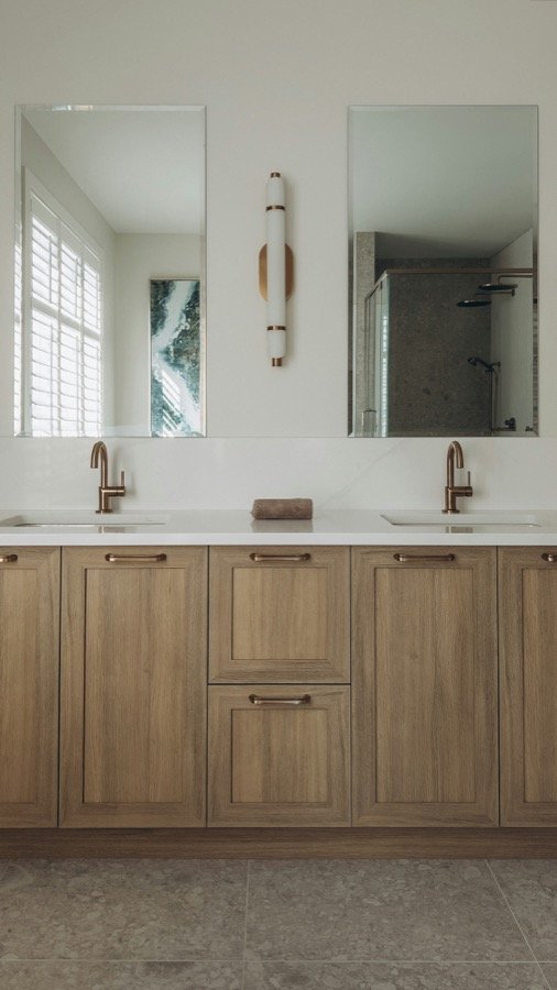 A bathroom vanity with brass fixtures lit by a wall sconce beside the mirror