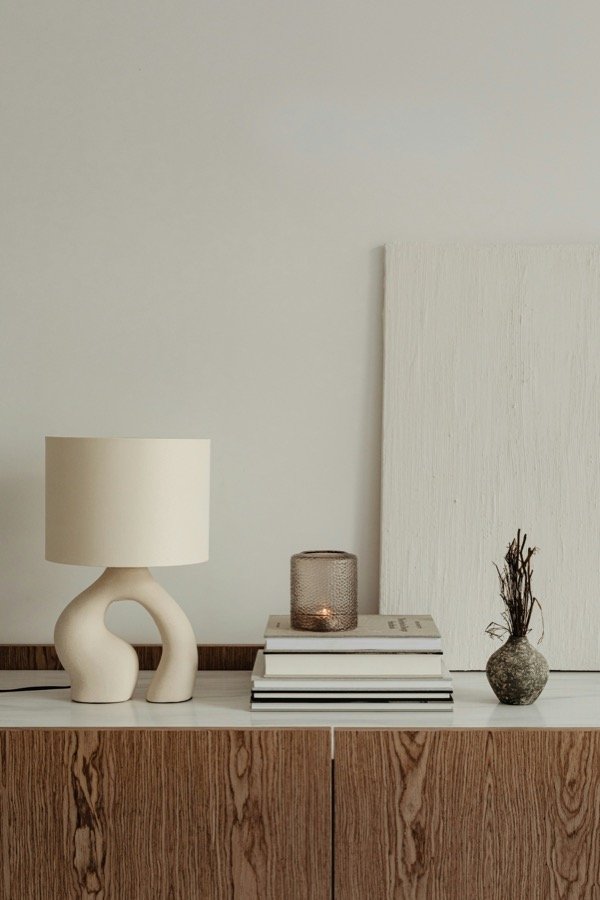 A sculptural white ceramic table lamp on a wooden credenza